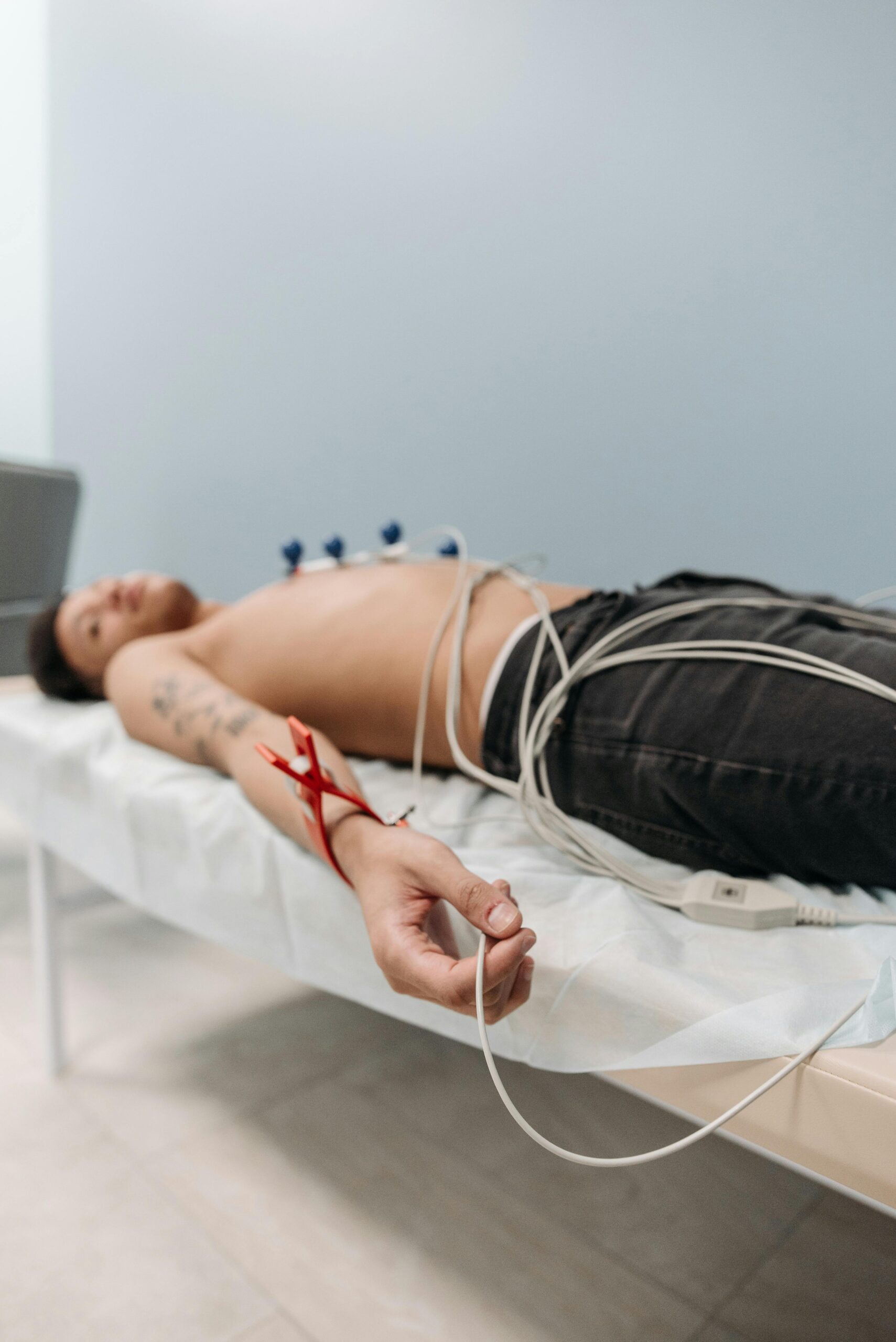 Shirtless male patient lying on bed connected to ECG machine for cardiogram.