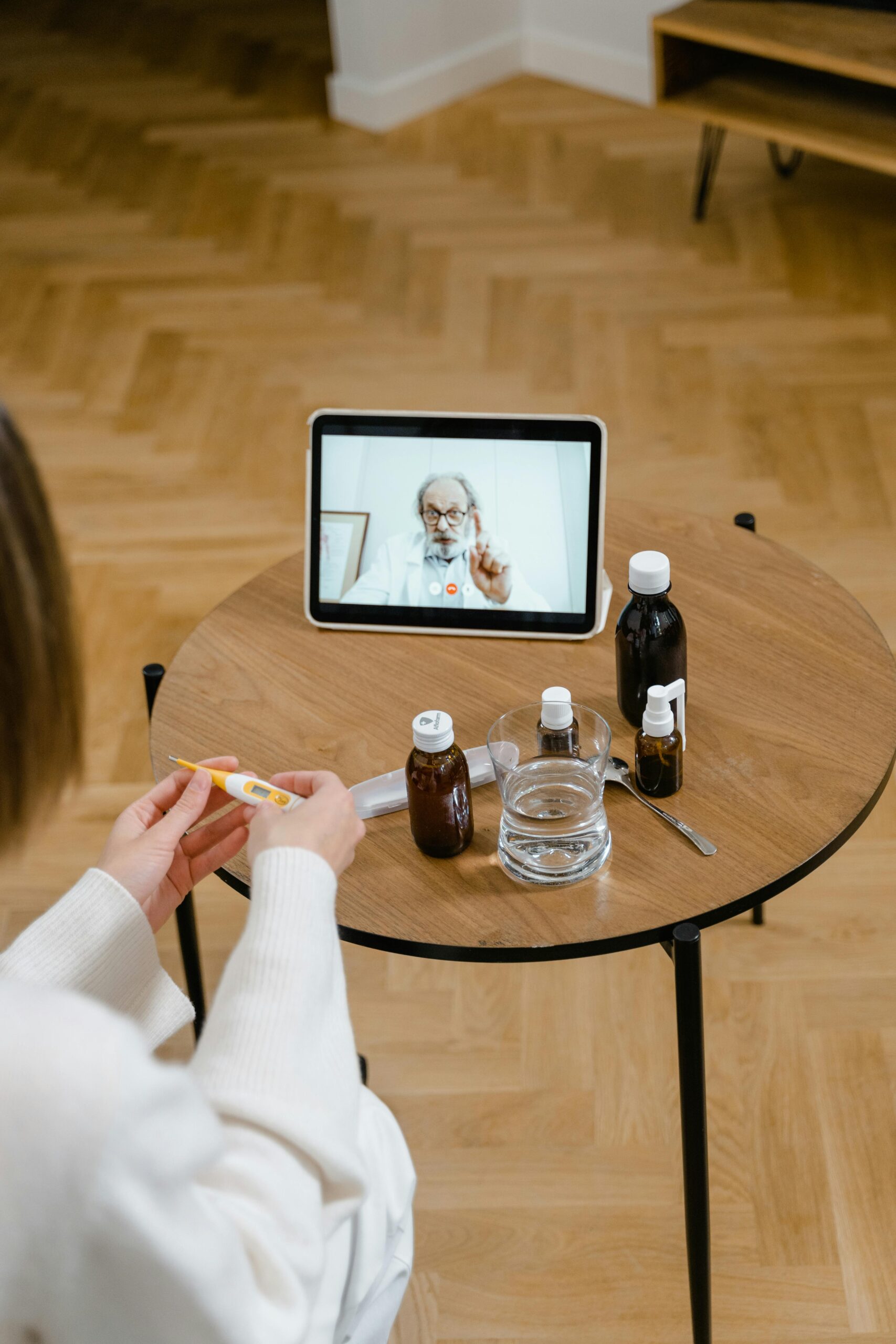 Woman in virtual consultation with doctor via tablet while holding a thermometer.